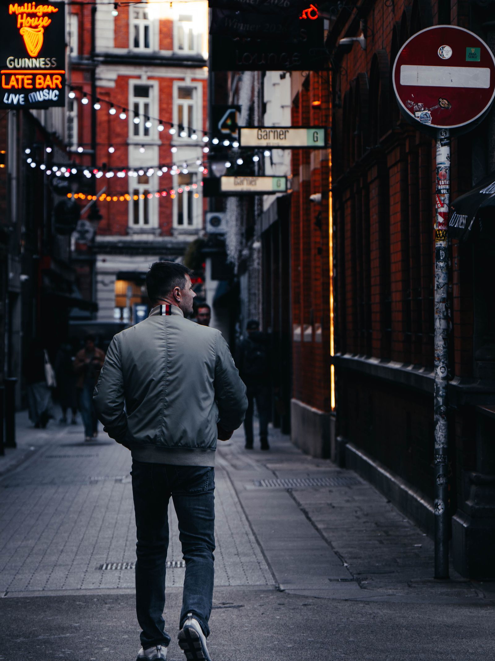 A man in a grey jacket walking away down a narrow Dublin street lined with pubs.