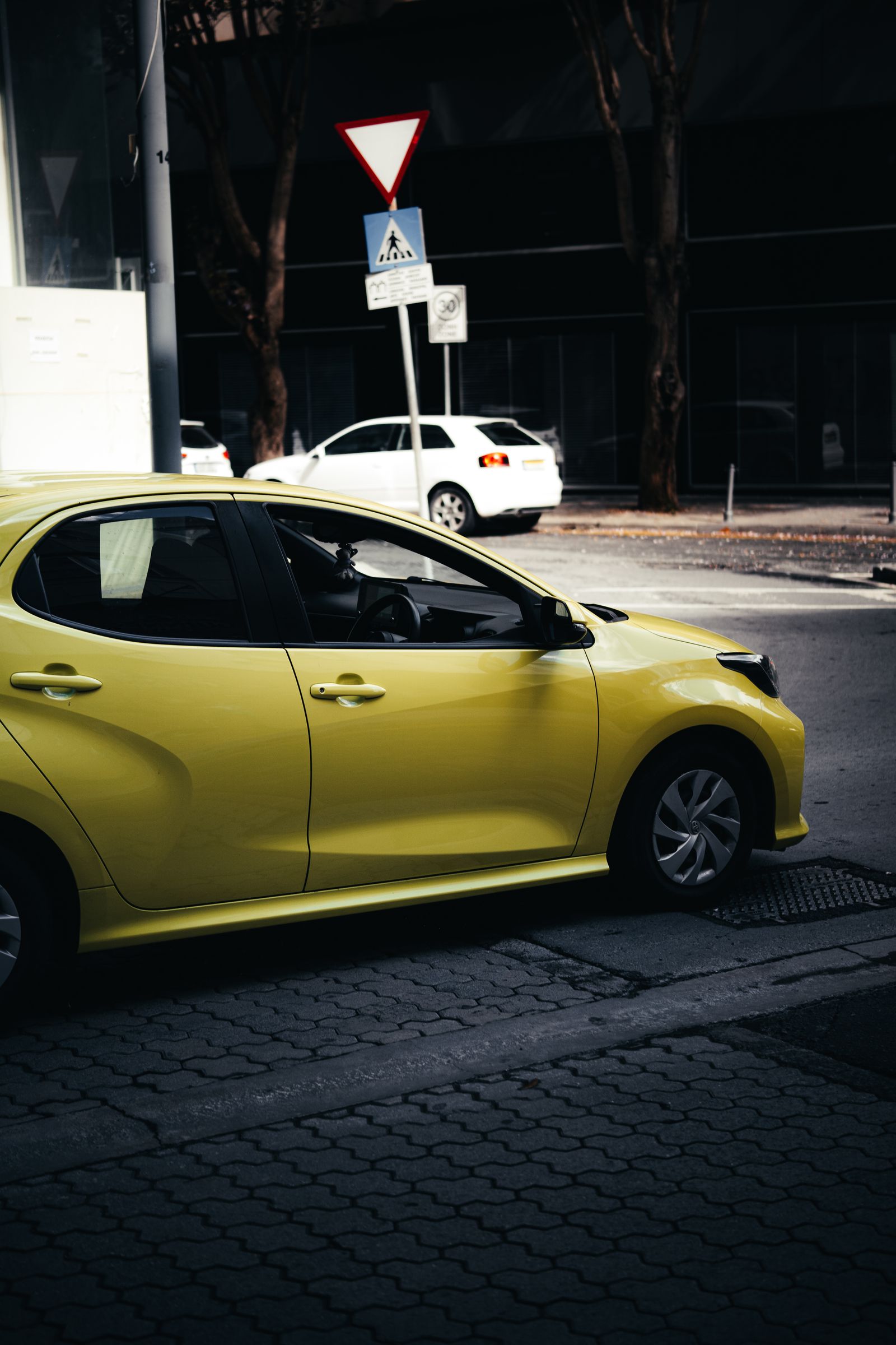 A yellow hatchback parked beside a give-way sign.