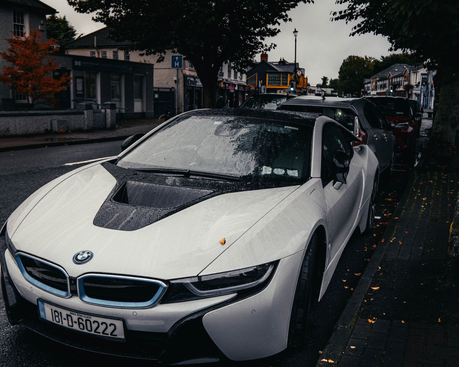 A white BMW i8 parked at the kerb on an overcast street, rain on the bonnet.