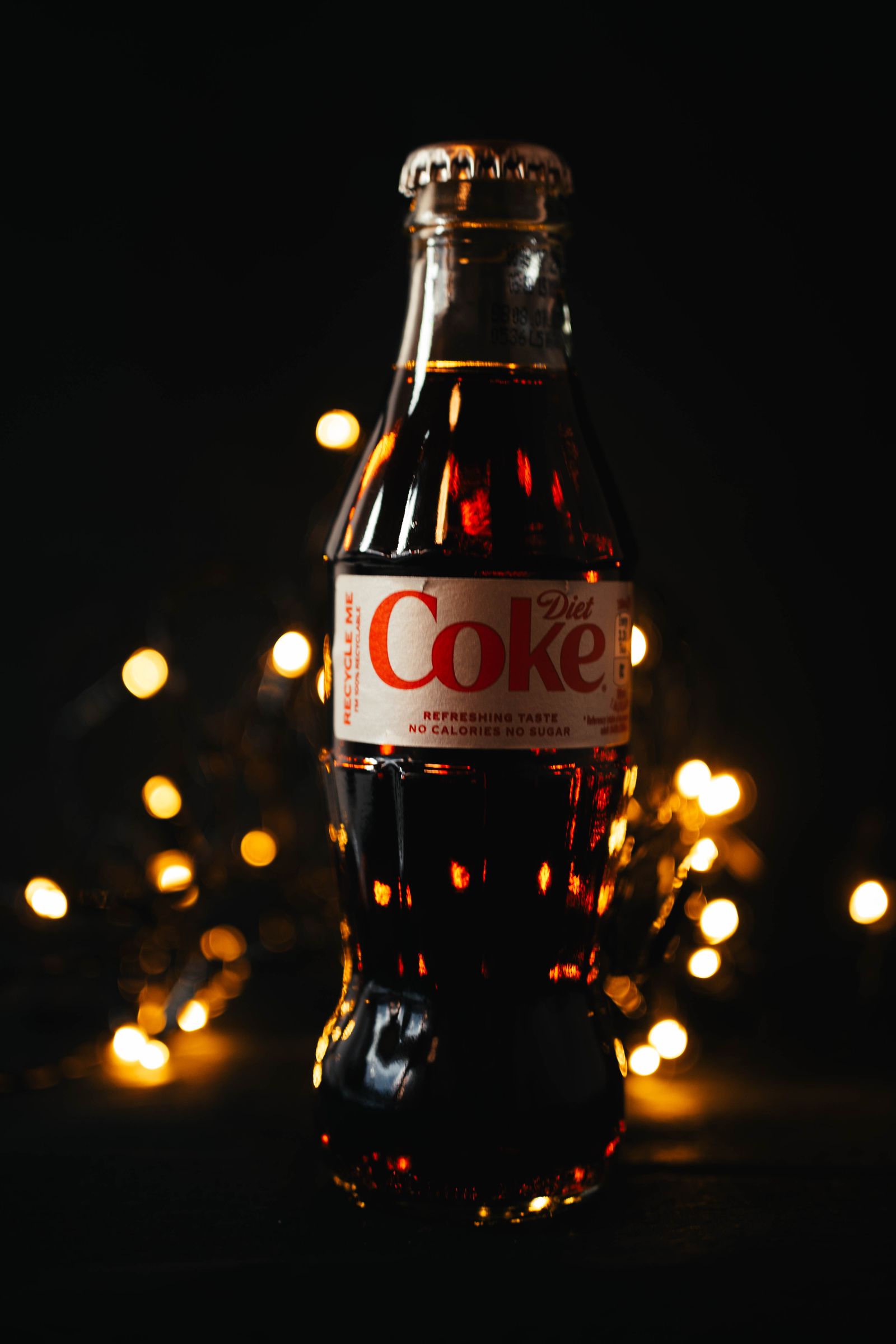 A Diet Coke bottle lit from behind, fairy lights glowing around its base.