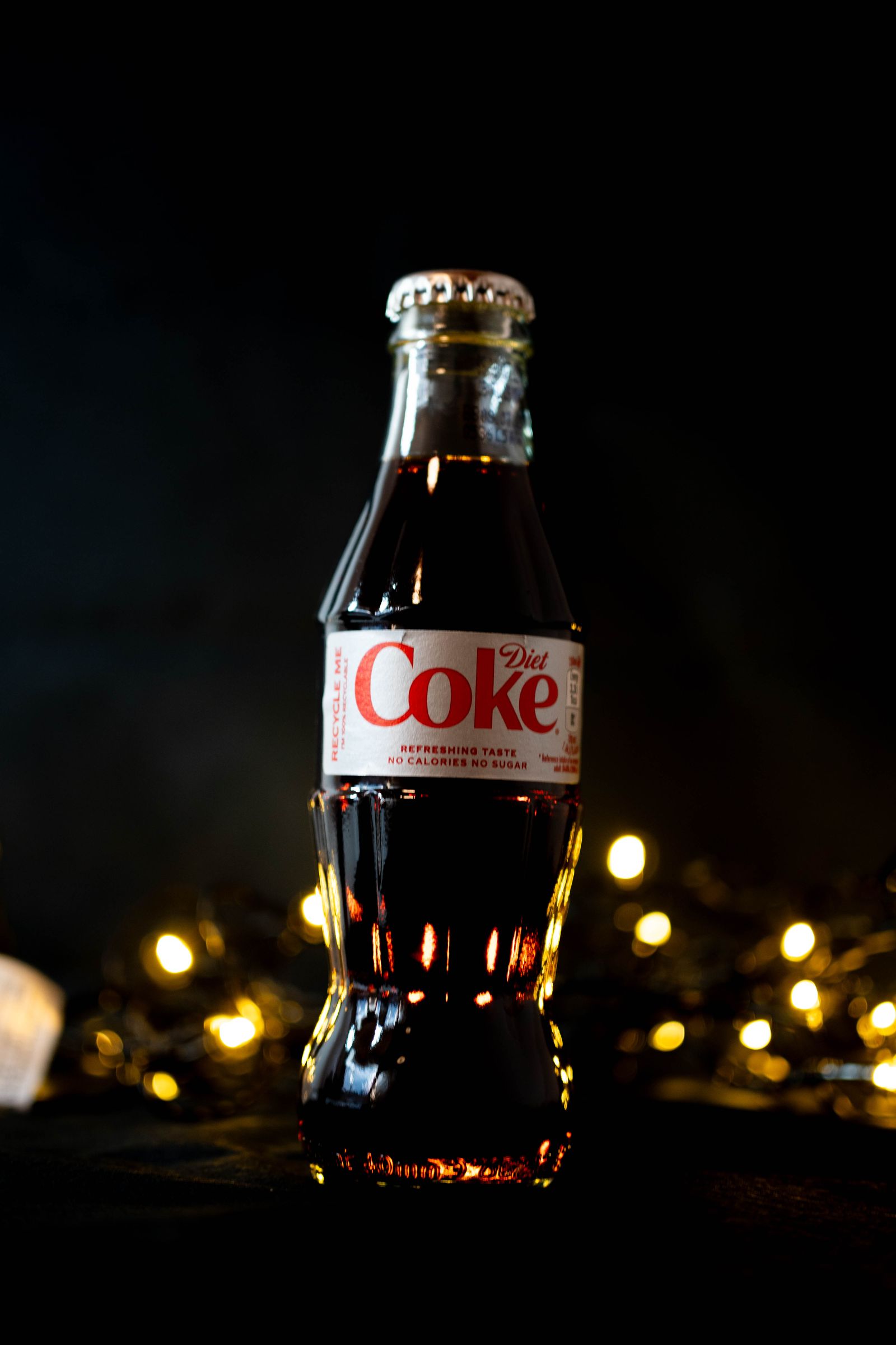 A Diet Coke bottle on black with a string of fairy lights below.