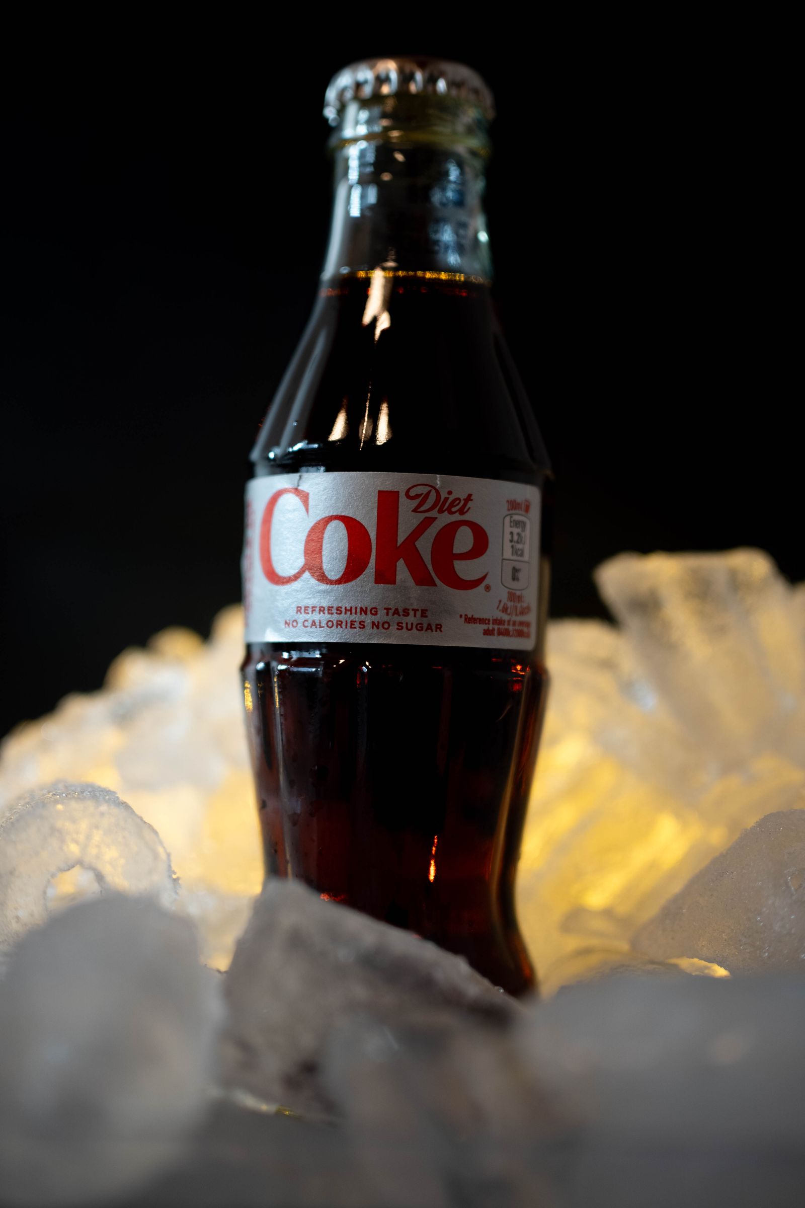A Diet Coke bottle standing in brightly lit crushed ice.