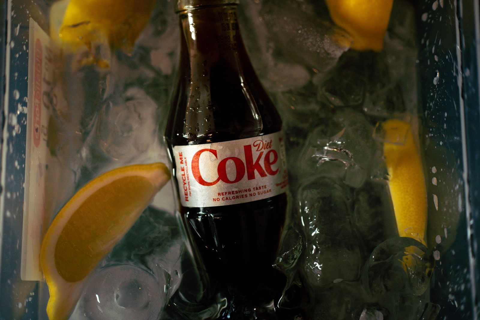 A Diet Coke bottle among ice and lemon slices, seen from above.