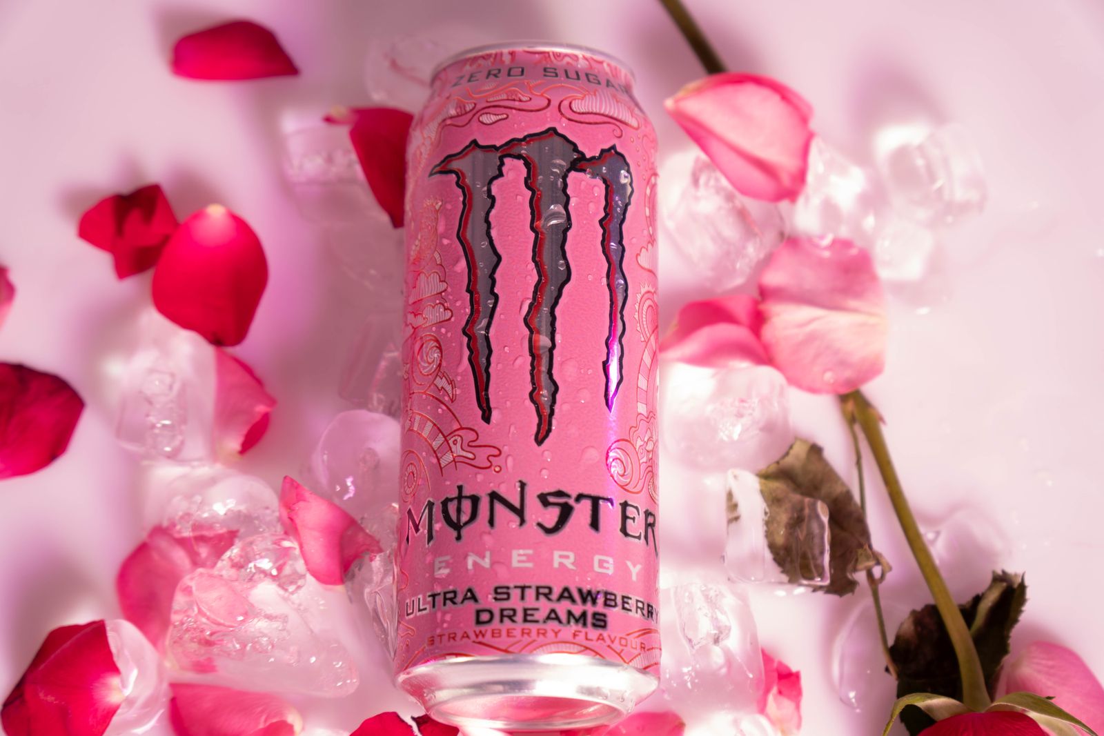 The can upright among ice cubes, rose petals and a rose stem.