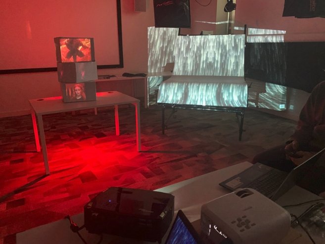Projector testing in a dark room lit red, with stacked screens and projected texture on the wall.
