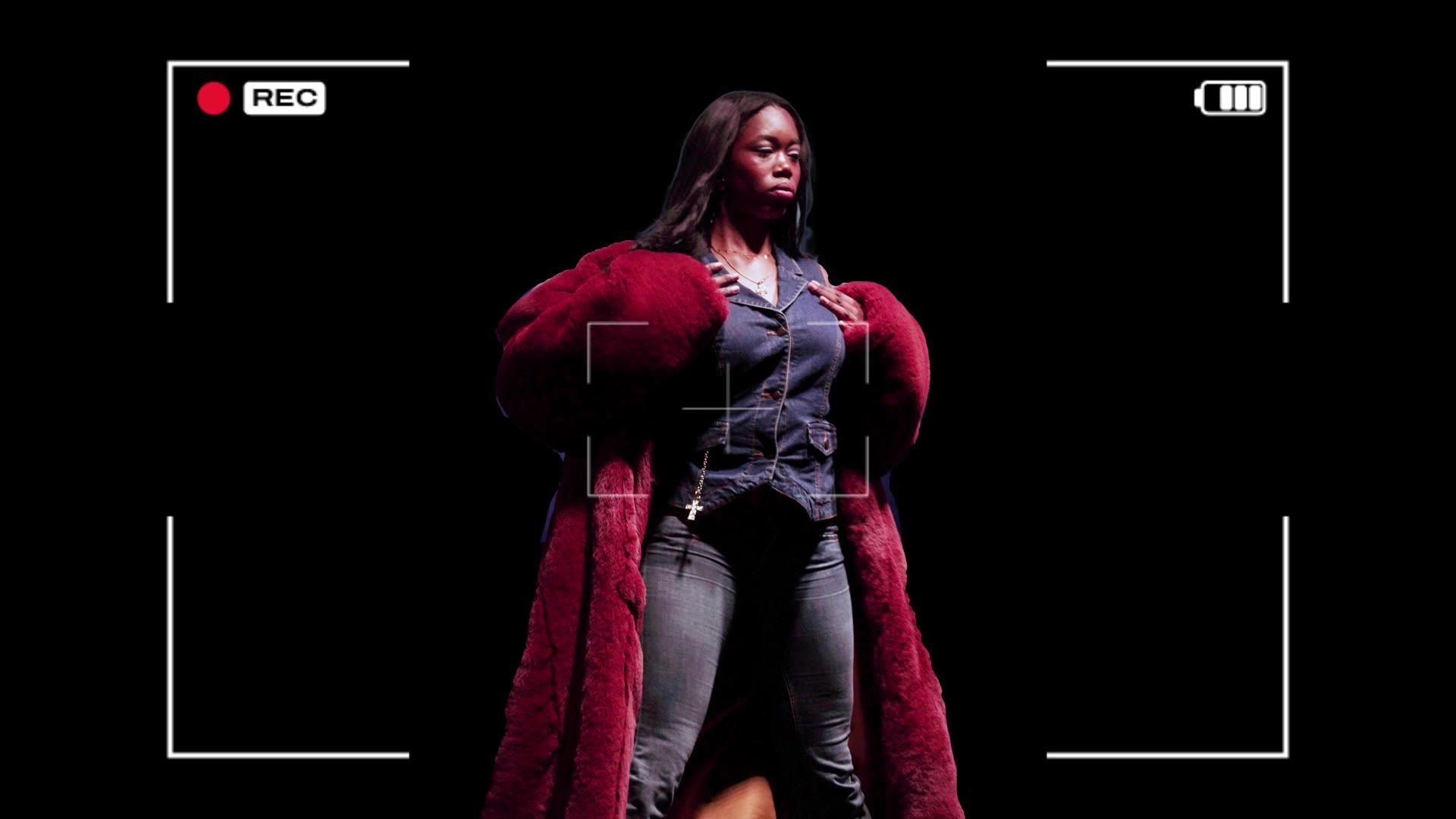 A model in a red faux-fur coat framed by a camera viewfinder overlay, from the film’s motion graphics.